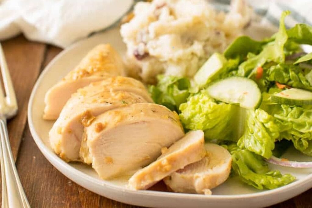Slices of garlic chicken with vegetables on the side.