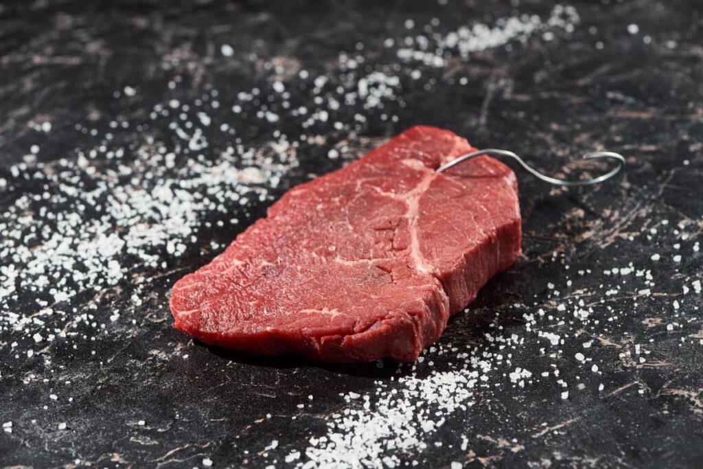 Raw meat on a dark table surrounded by salt.