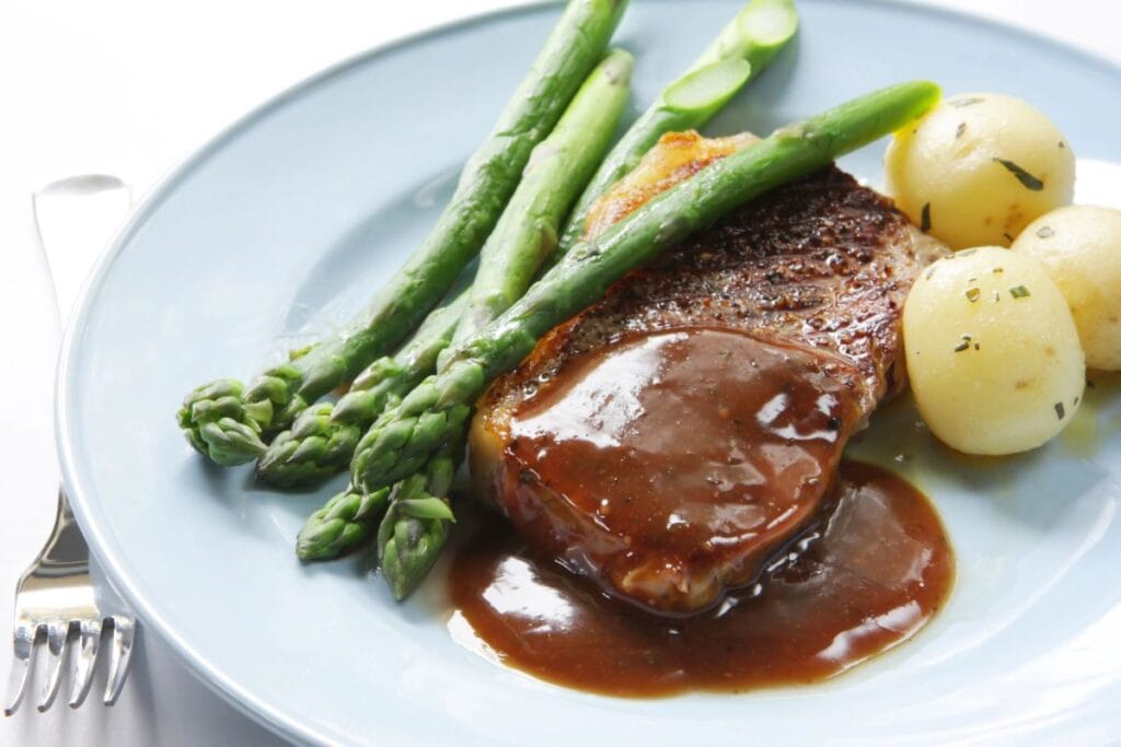 Steak and veggies on a white plate smothered in gravy.