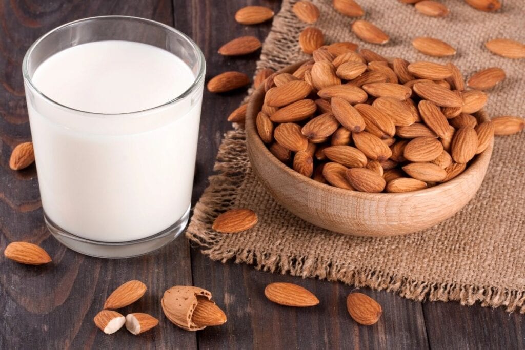 A glass of milk with almonds on the side.