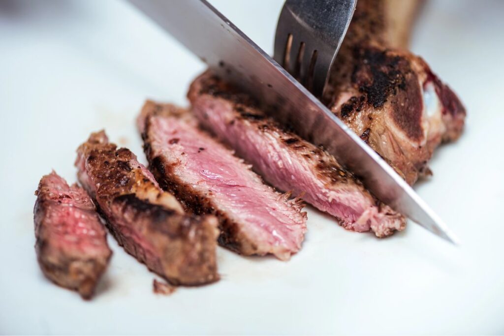 Meat getting sliced with a knife and fork on a white background.