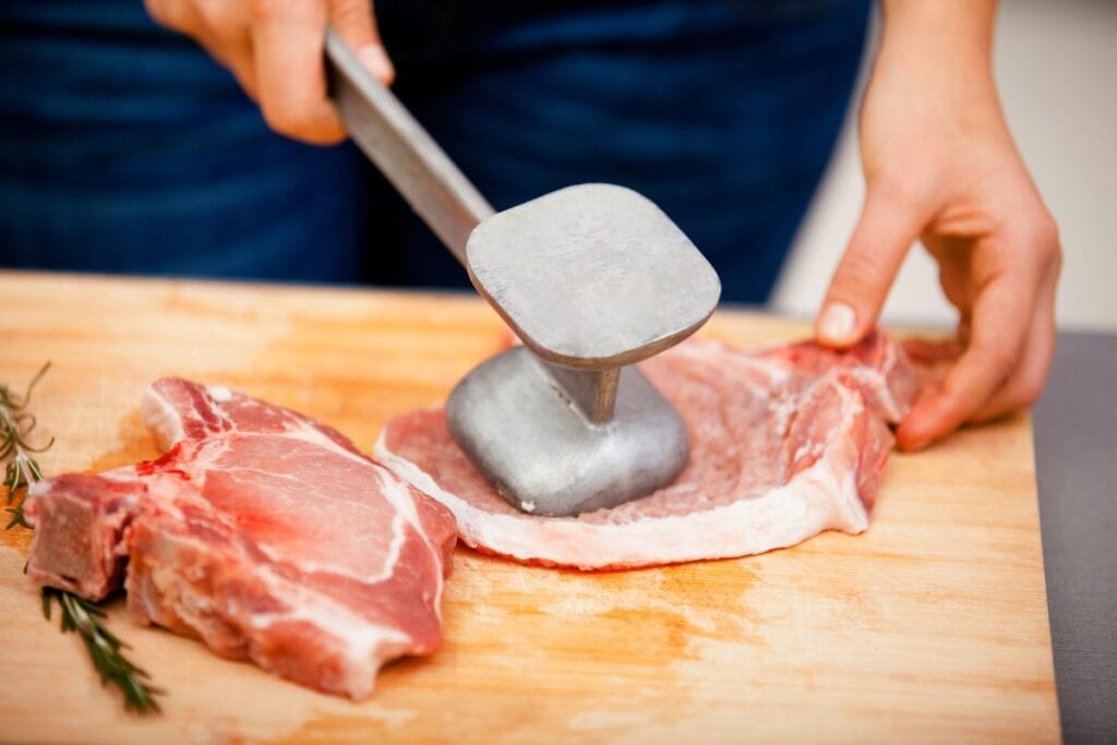 Tenderizing meat with a mallet on a cutting board.