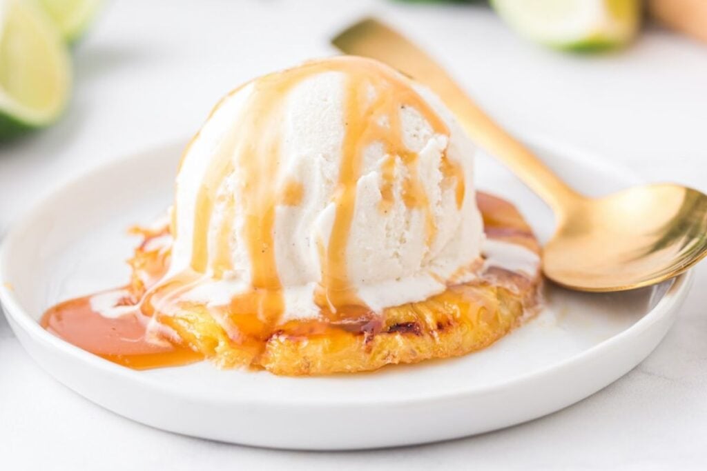 Grilled pineapple with ice cream on top on white plate.