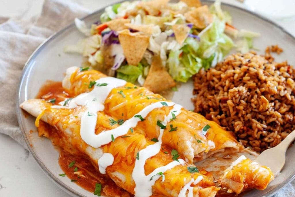 Enchiladas topped with cheese with rice and salad on a plate.