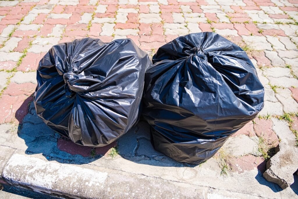 Two black garbage bags on the sidewalk.
