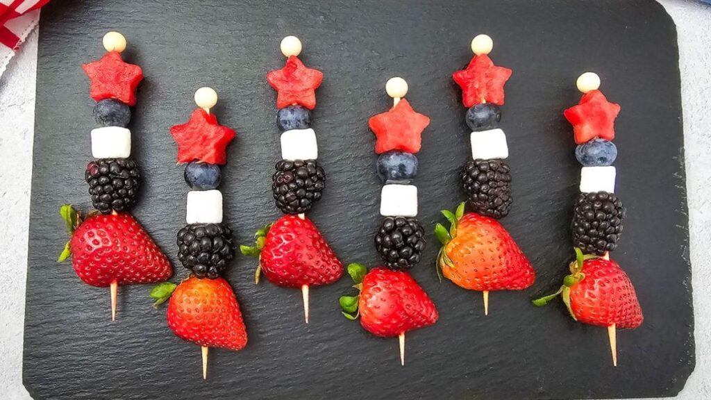 Patriotic fruit kebabs on cutting board.