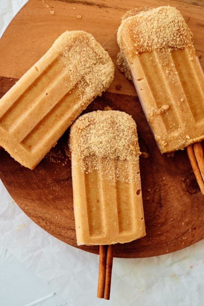Pumpkin pie popsicles with cinnamon stick on cutting board.