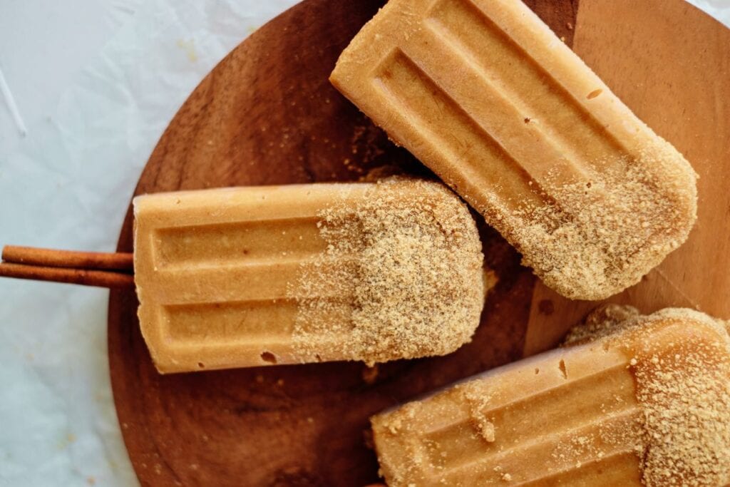 Pumpkin popsicles on a wood cutting board.