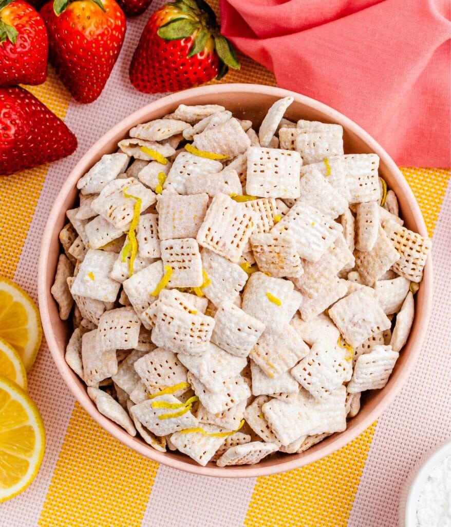 Strawberry lemonade chex mix in pink bowl with strawberries and lemons in the background.