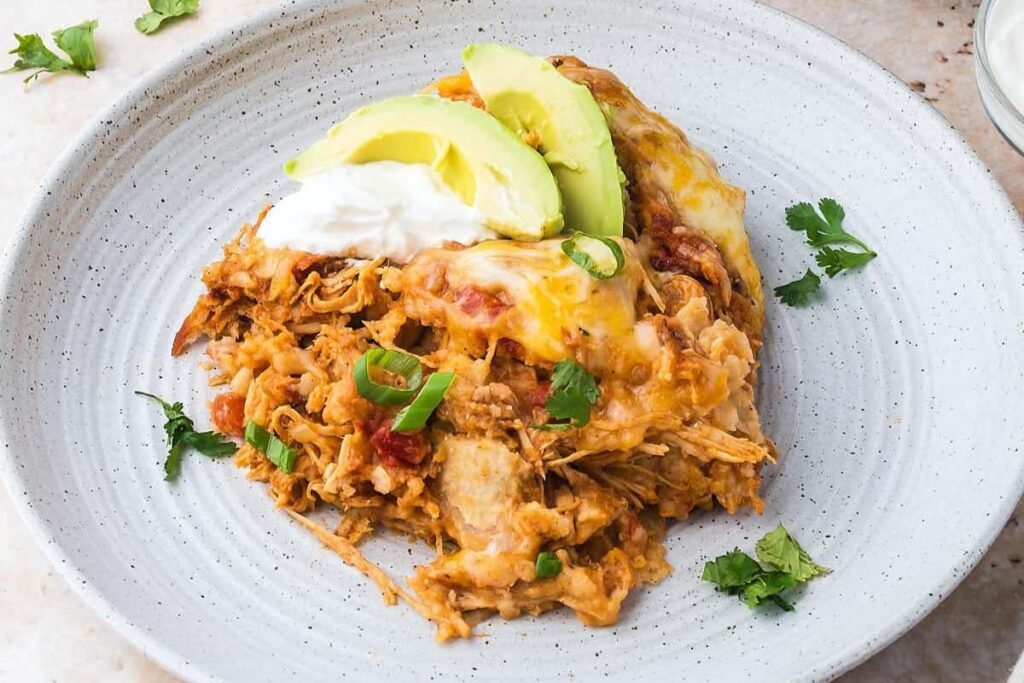 Chicken enchilada with sliced avocados on a plate.