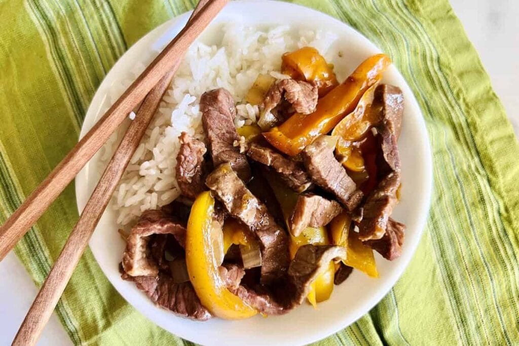 A bowl of rice with pepper steak.