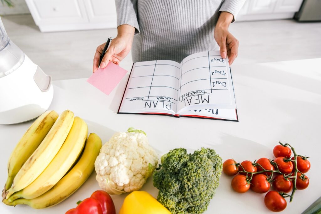 Person meal planning in kitchen with vegetables and bananas on table.