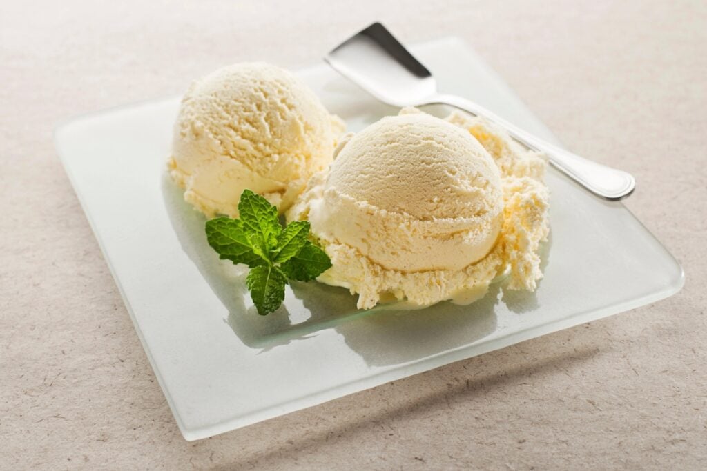 Vanilla ice cream on a white plate topped with a fresh mint leaf.