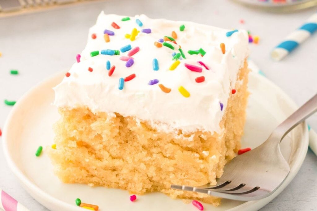 A slice of vanilla cake with sprinkles on top.