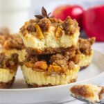 Mini apple crisp cheesecakes on a round plate.
