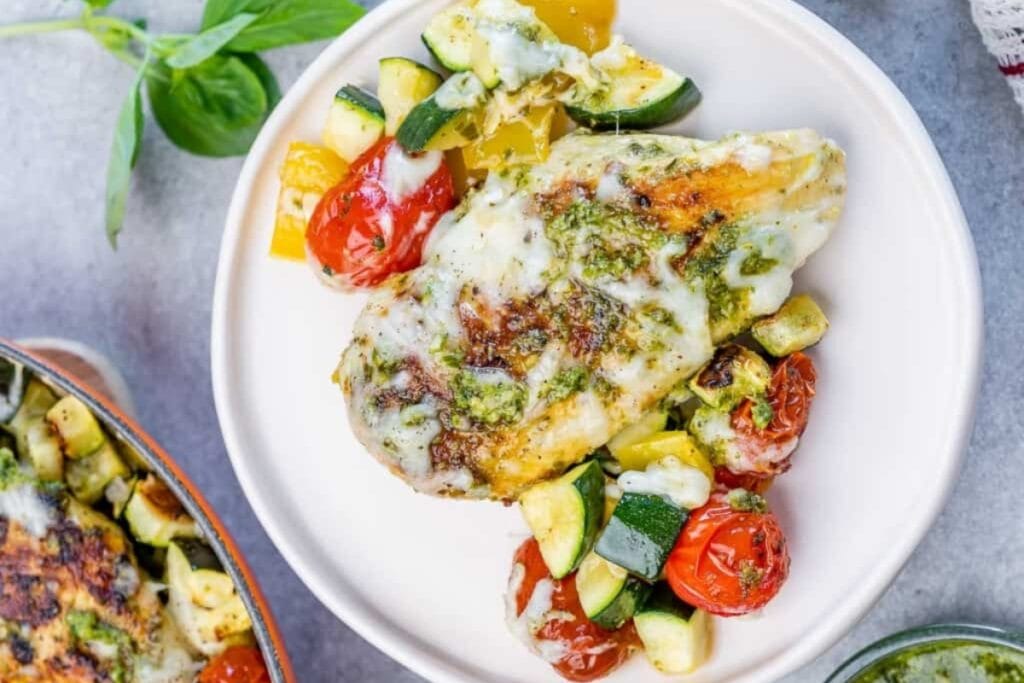 Baked pesto chicken with vegetables on a round white plate.