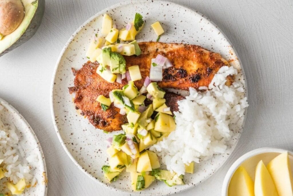 Blackened fish with mango salsa and rice on a round plate.