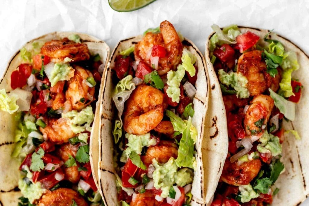 Three blackened shrimp tacos placed on parchment paper.