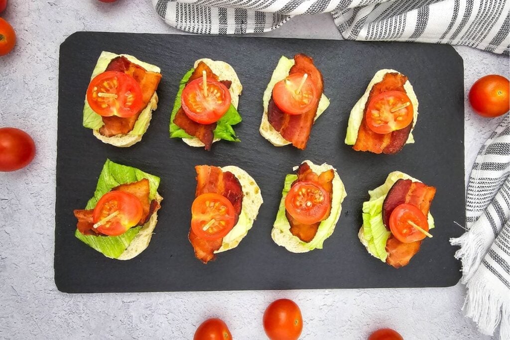 Mini BLT bites arranged on a black slate serving board.