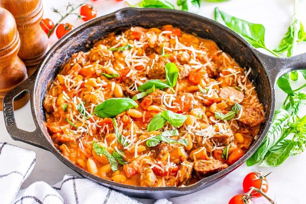 Cannellini beans and sausage topped with fresh basil in a skillet.