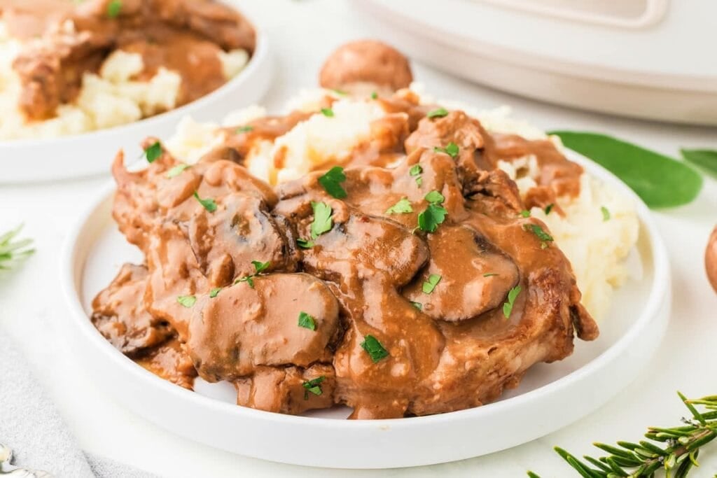 Crockpot pork chops with mushroom gravy served on a white plate.