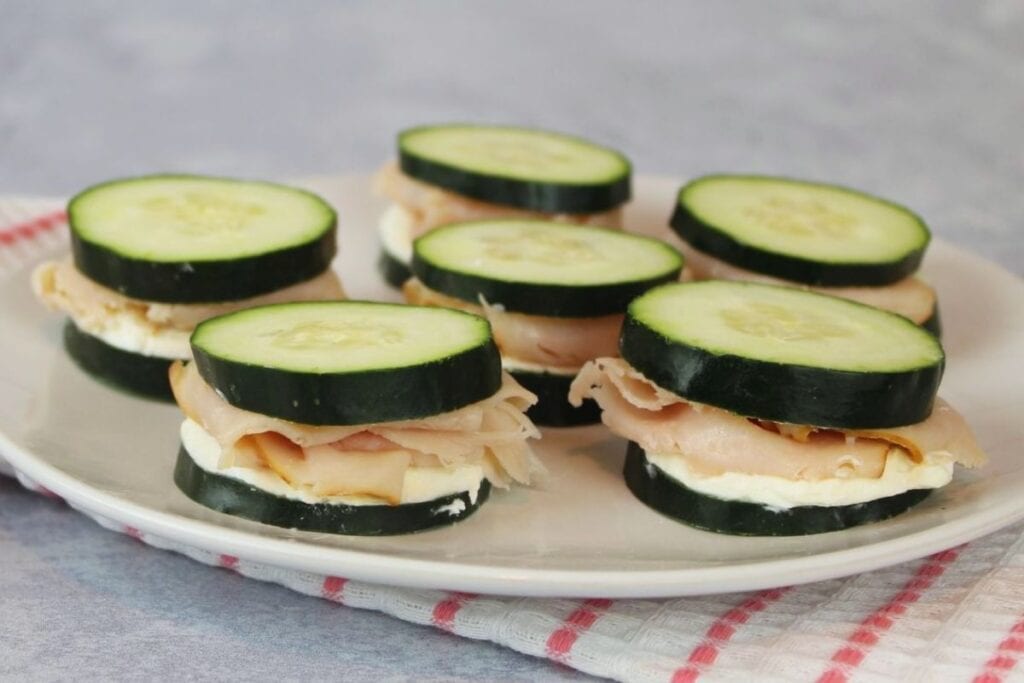 Mini cucumber sandwiches on white plate.
