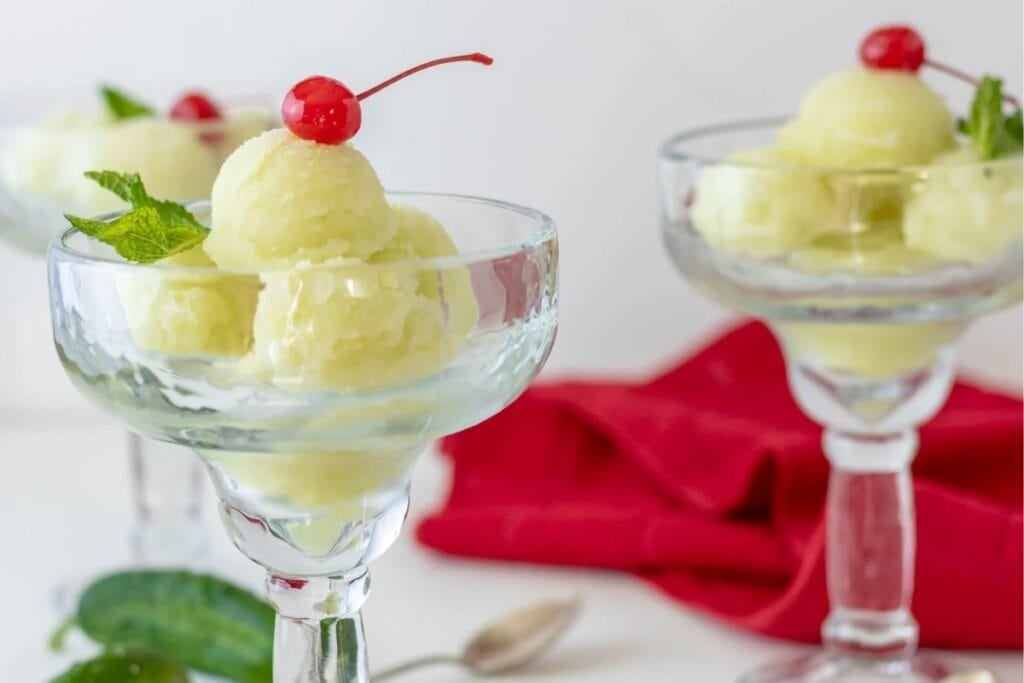 Three glasses of cucumber sorbet topped with mint leaves and cherries.