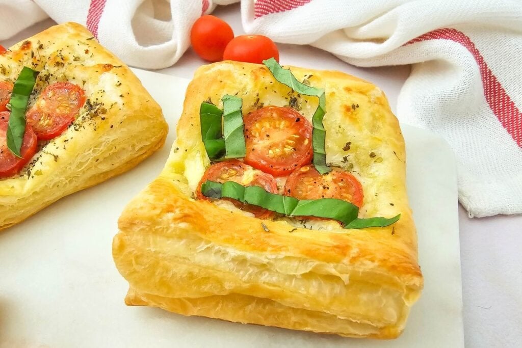 Close-up of golden tomato puff pastry tartlets with herbs on a white plate.