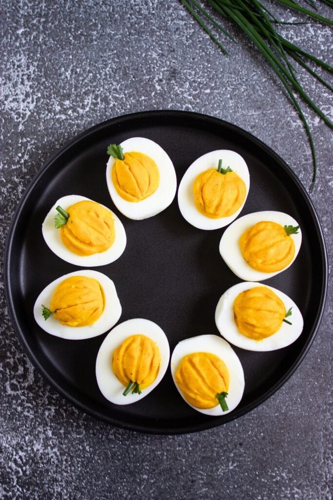 Easy fall appetizer with pumpkin deviled eggs on a black plate.