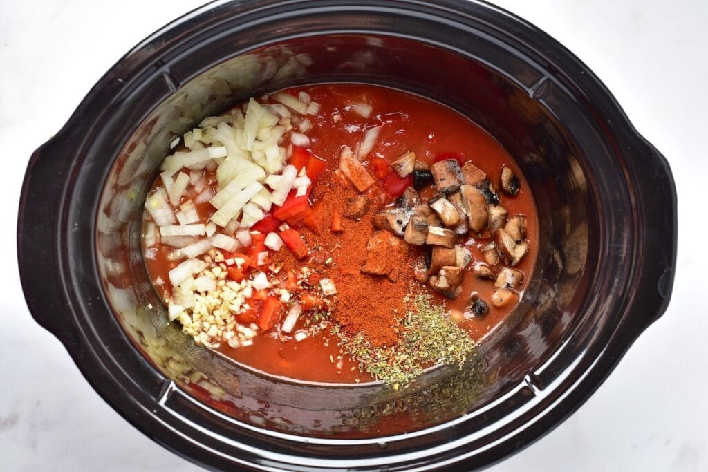 Adding chopped mushrooms, onions, and bell peppers into a slow cooker for Italian chicken cacciatore.
