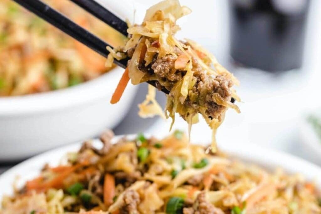 Egg roll in a white bowl picked up with chopsticks.
