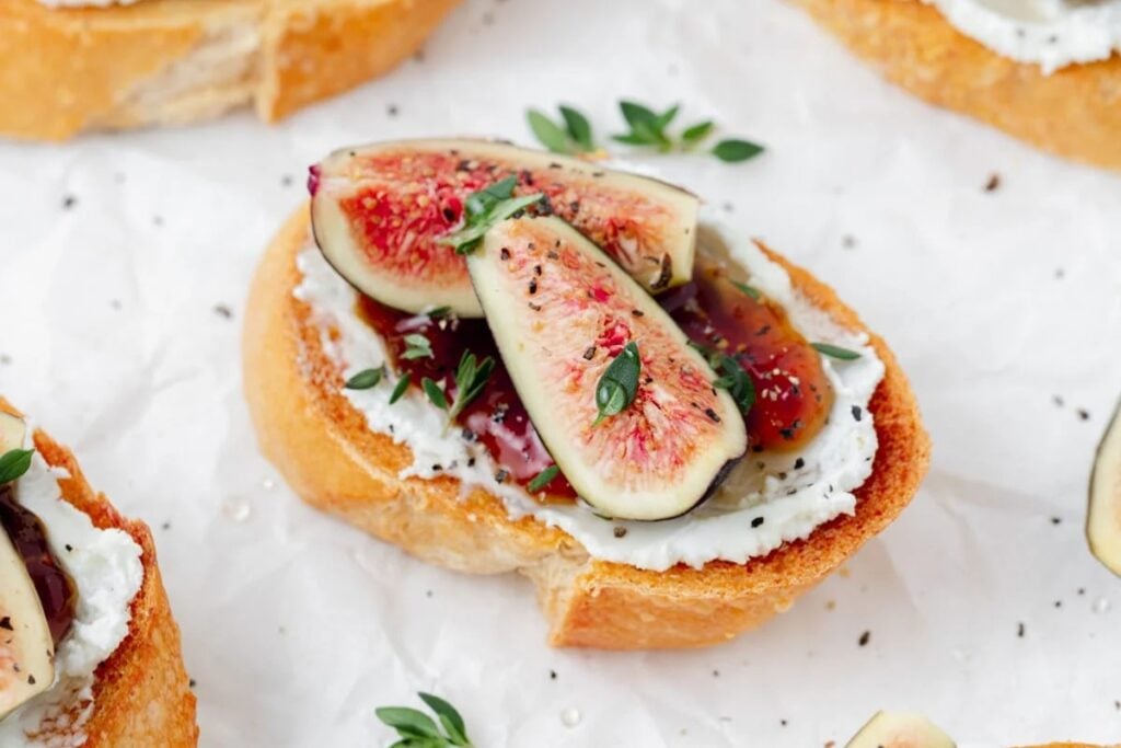 Fig and goat cheese crostini on white parchment paper.