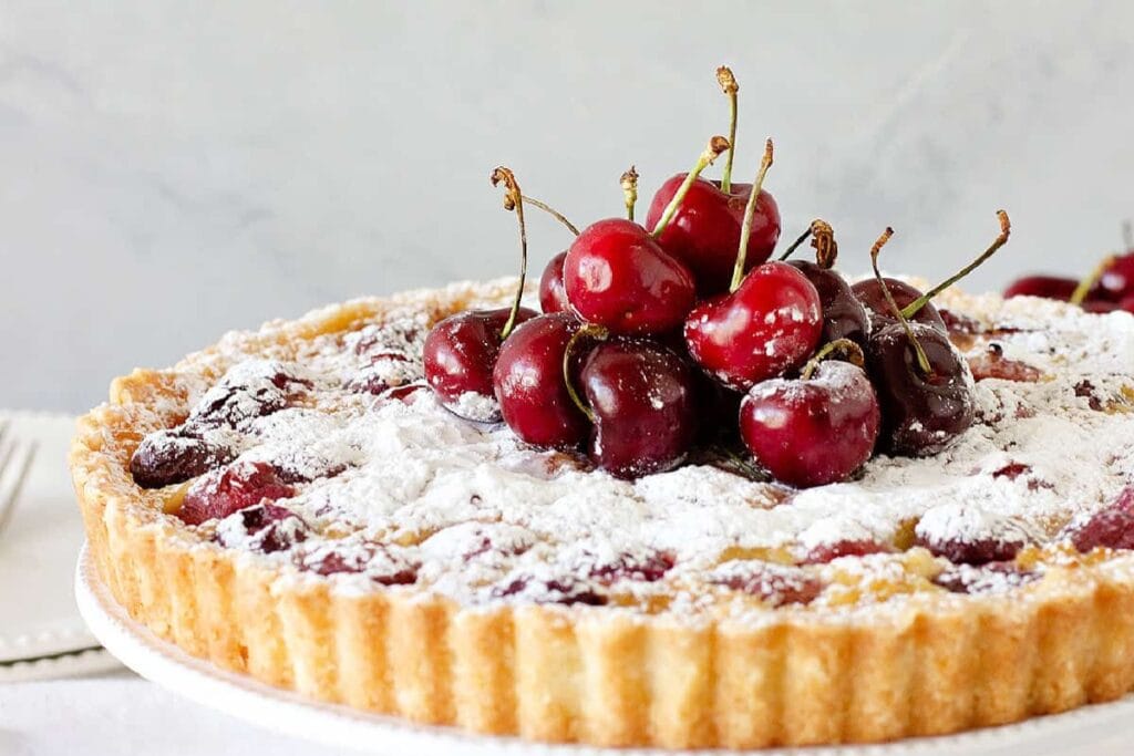 Fresh cherry tart on a white round plate, with glossy cherries on top.