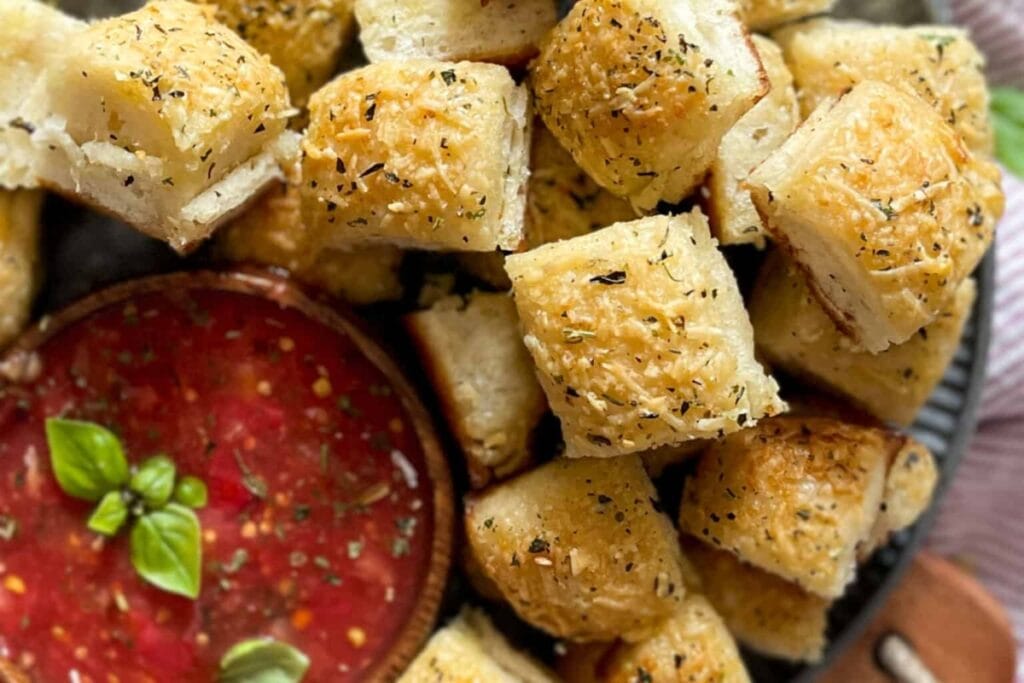 Garlic parmesan bread bites arranged around a bowl of marinara sauce.