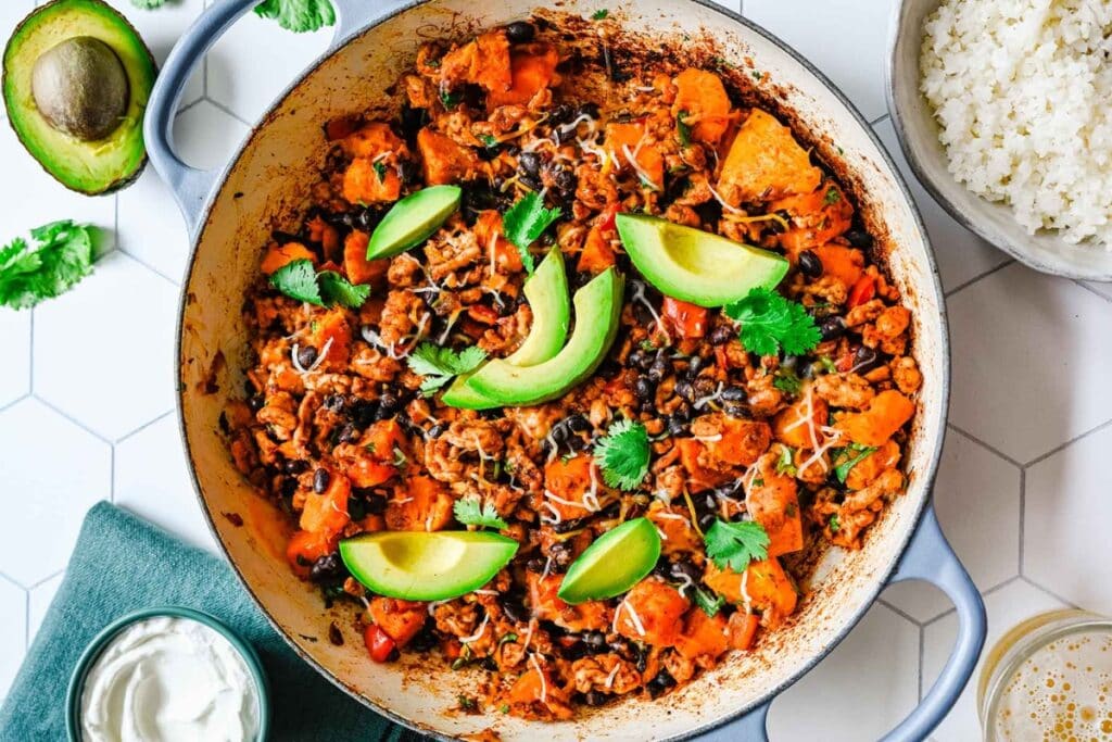 Ground turkey and sweet potato skillet topped with herbs and avocado.