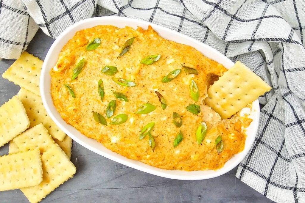 Hot crab dip in a rectangular baking dish served with crackers.
