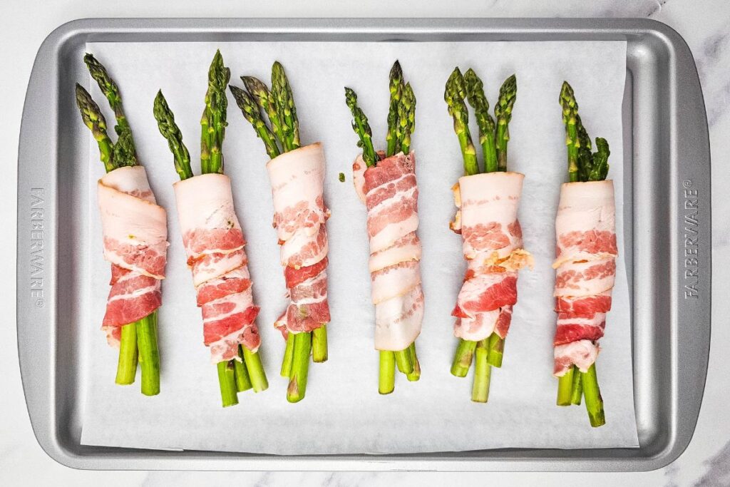 Raw asparagus wrapped in bacon on an oven tray.