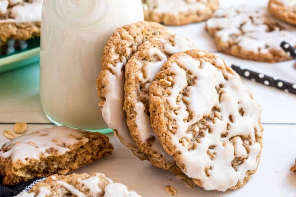 Iced oatmeal cookies leaning against a bottle of milk.
