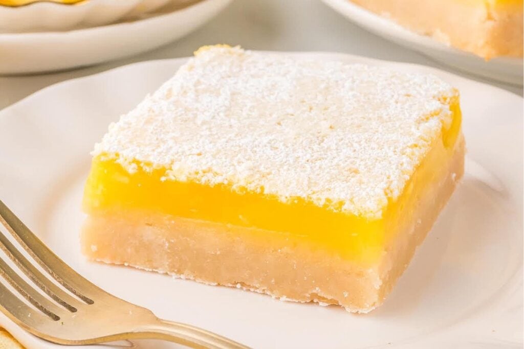 Lemon bar on a white plate, dusted with powdered sugar.