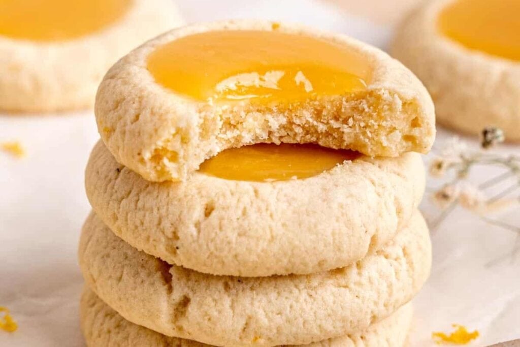 Stack of lemon curd thumbprint cookies on parchment paper.