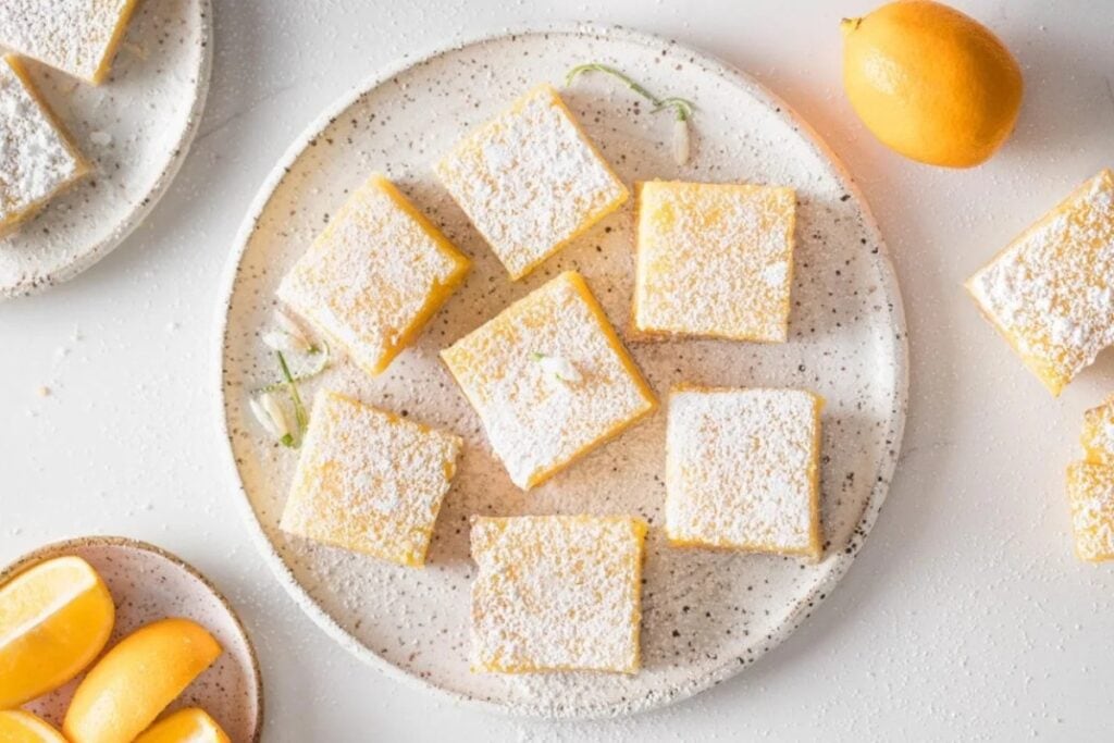 Meyer lemon bars on a round plate, dusted with powdered sugar.