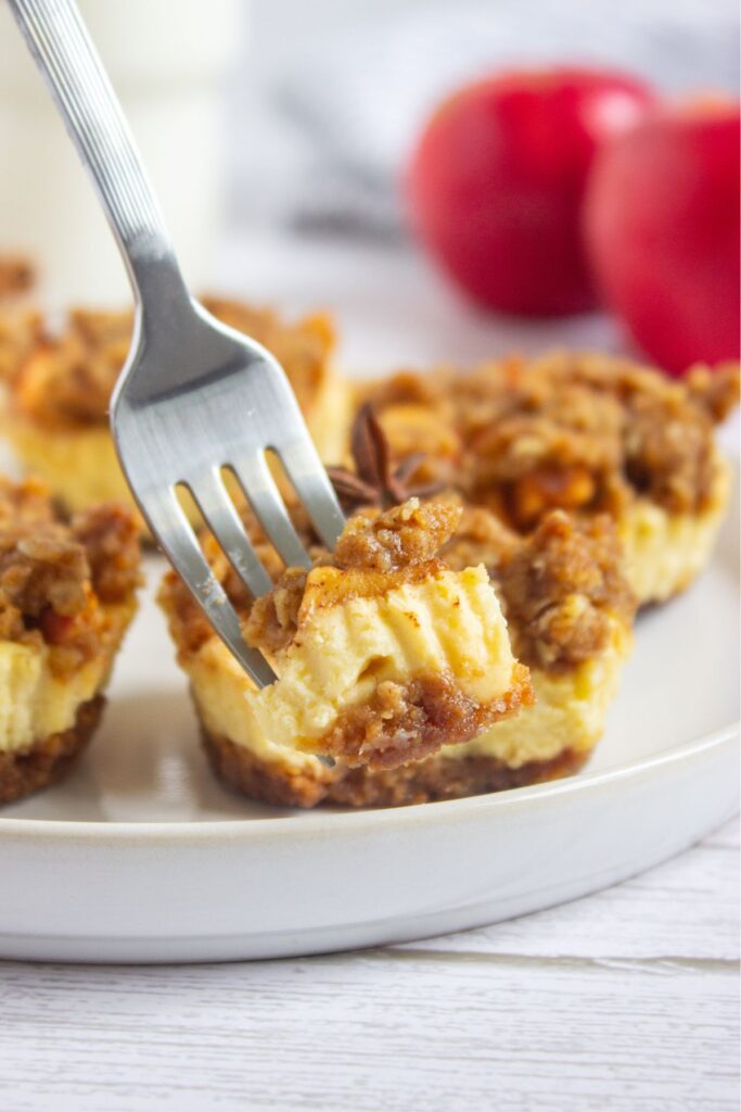 Mini apple crisp cheesecakes on a round plate, one with a fork in it.