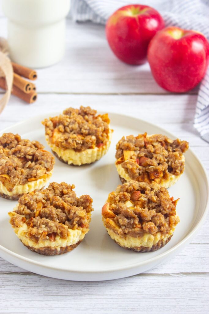 Mini apple crisp cheesecakes on a round plate.