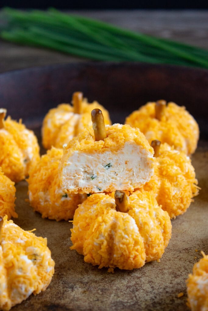 Mini Pumpkin Cheese Ball coated in shredded cheddar and topped with pretzel stems