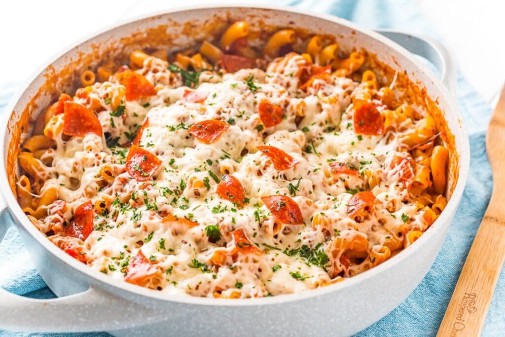 Cheesy pizza pasta cooked in a white skillet, topped with melted cheese and pepperoni.