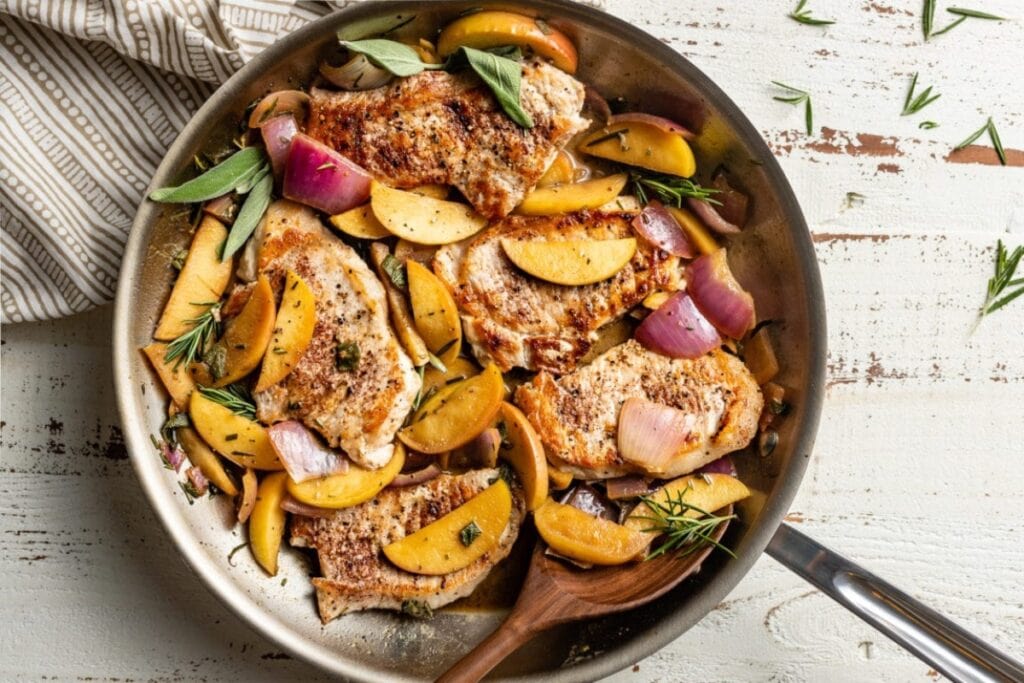 Pork chops with apples cooked in a skillet.