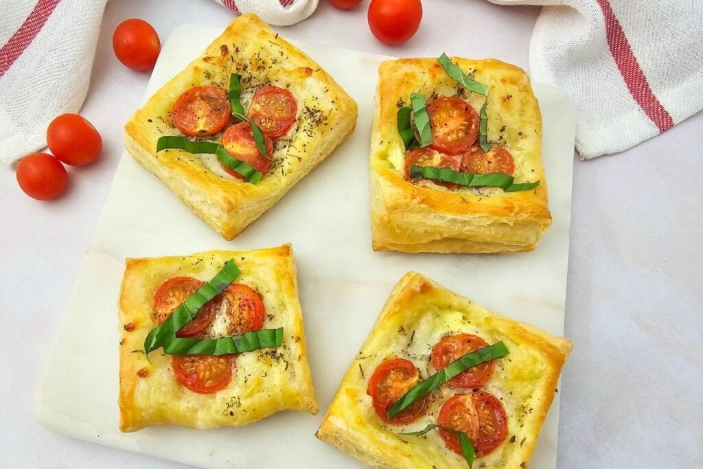 Puff pastry tomato tartlets on a white plate.