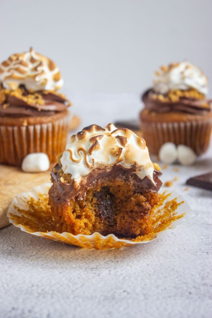 Bitten pumpkin cupcake with toasted marshmallow frosting on cement counter.