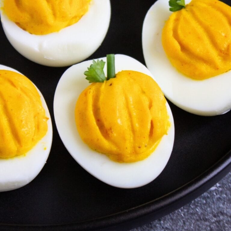 Close-up of pumpkin deviled eggs on a black plate, an easy fall appetizer.
