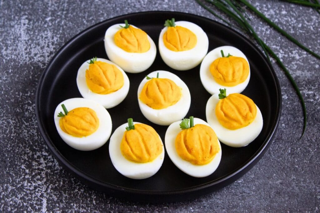 Easy fall appetizer with pumpkin deviled eggs on a black plate.
